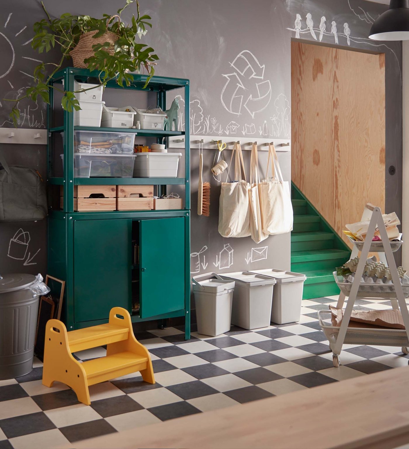 A hallwall with a chequerboard floor, green cupboards and three recycling containers lined up against the wall.