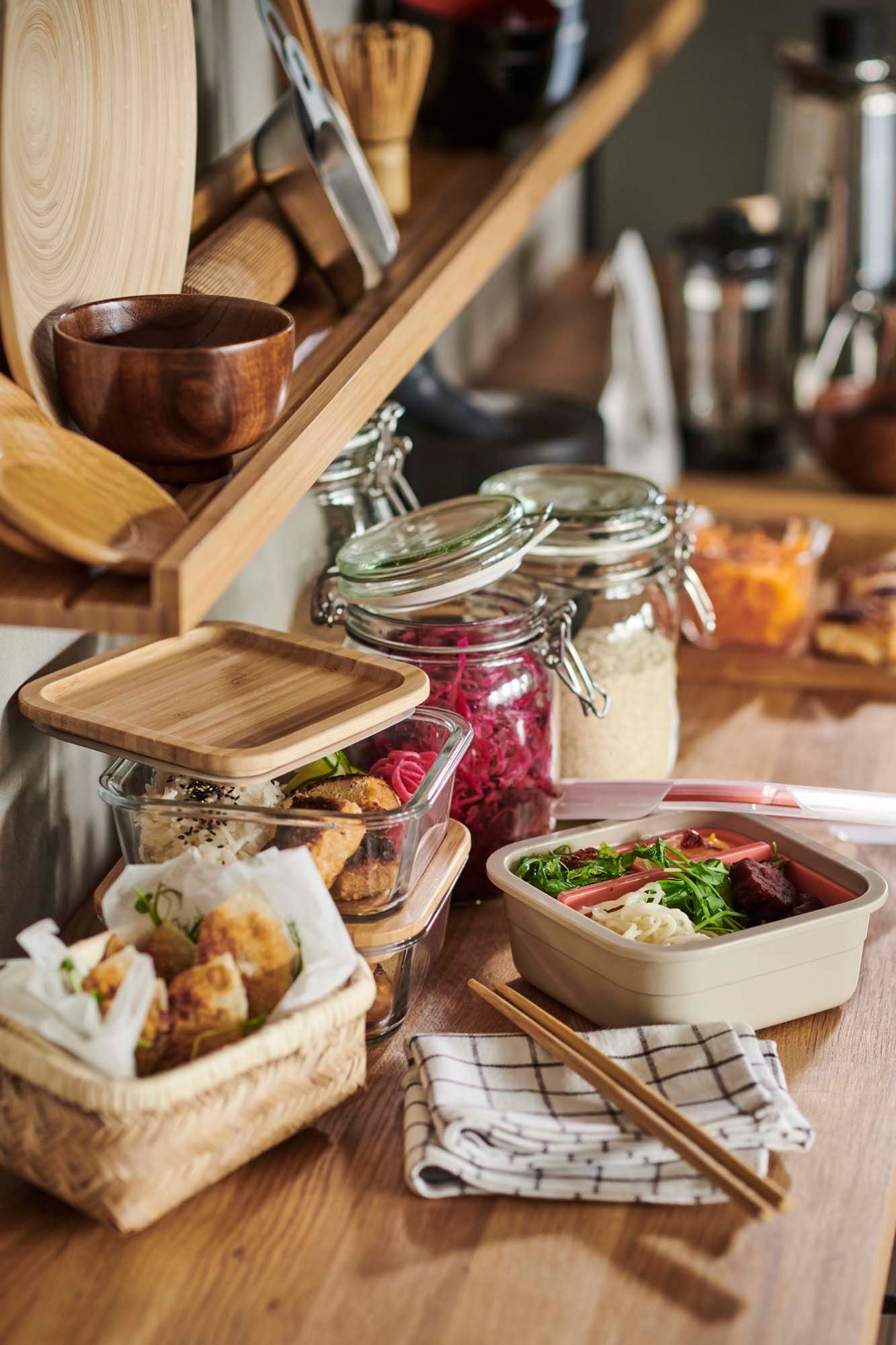 A selection of glass and bamboo food storage containers sits on a wooden kitchen worktop.