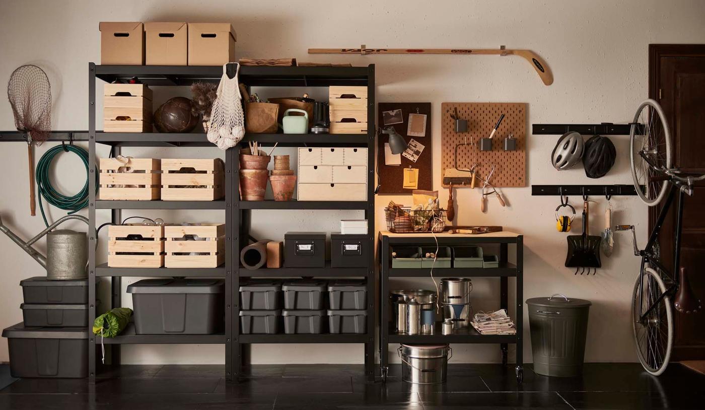 Black open shelving with storage containers, a trolley, pegboard for tools, and workbench in a black-and-white garage. 