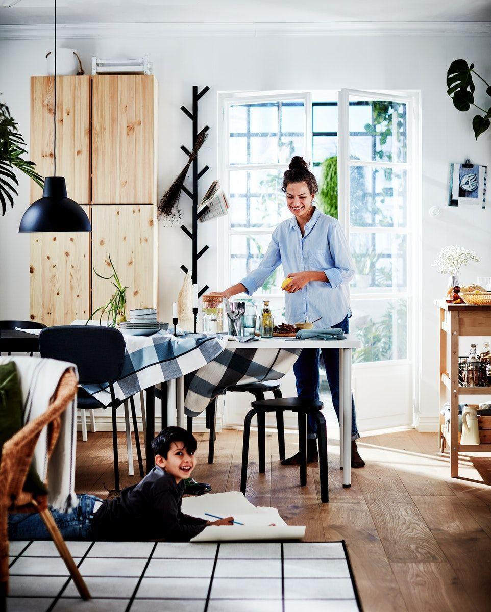 A woman is laying the dining room table and smiling. A boy is lying on the floor smiling and drawing.