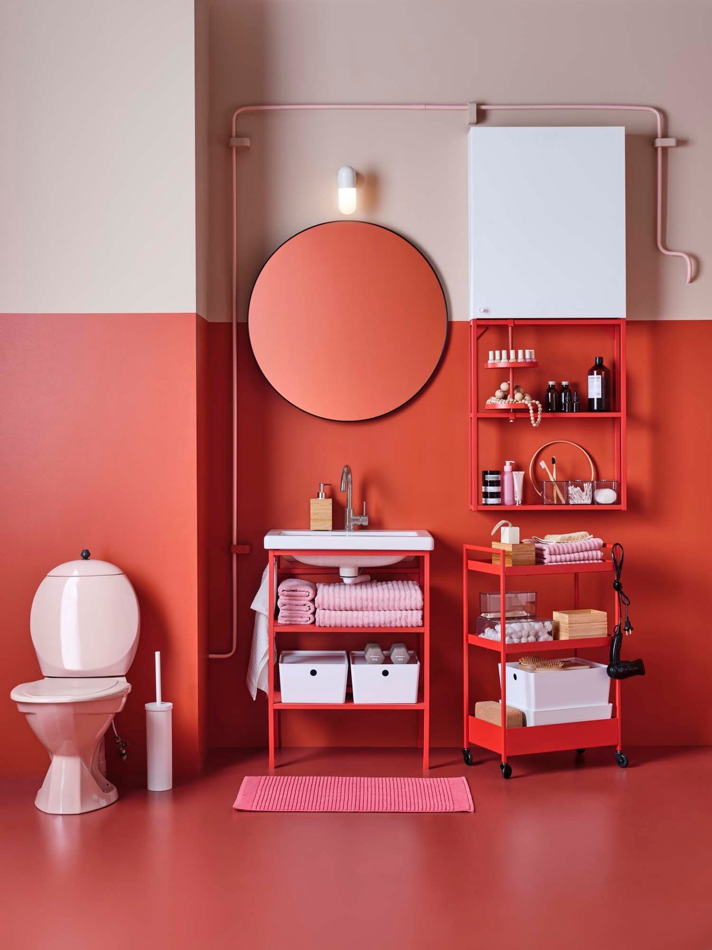 A red and white bathroom with red storage trolleys below a round mirror.