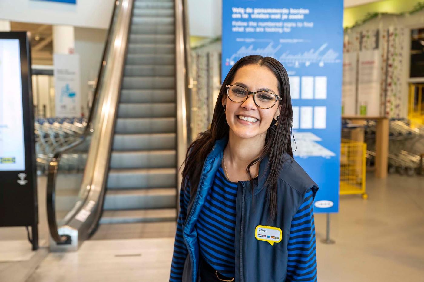 An IKEA co-worker smiles at the camera in the entrance of an IKEA store.