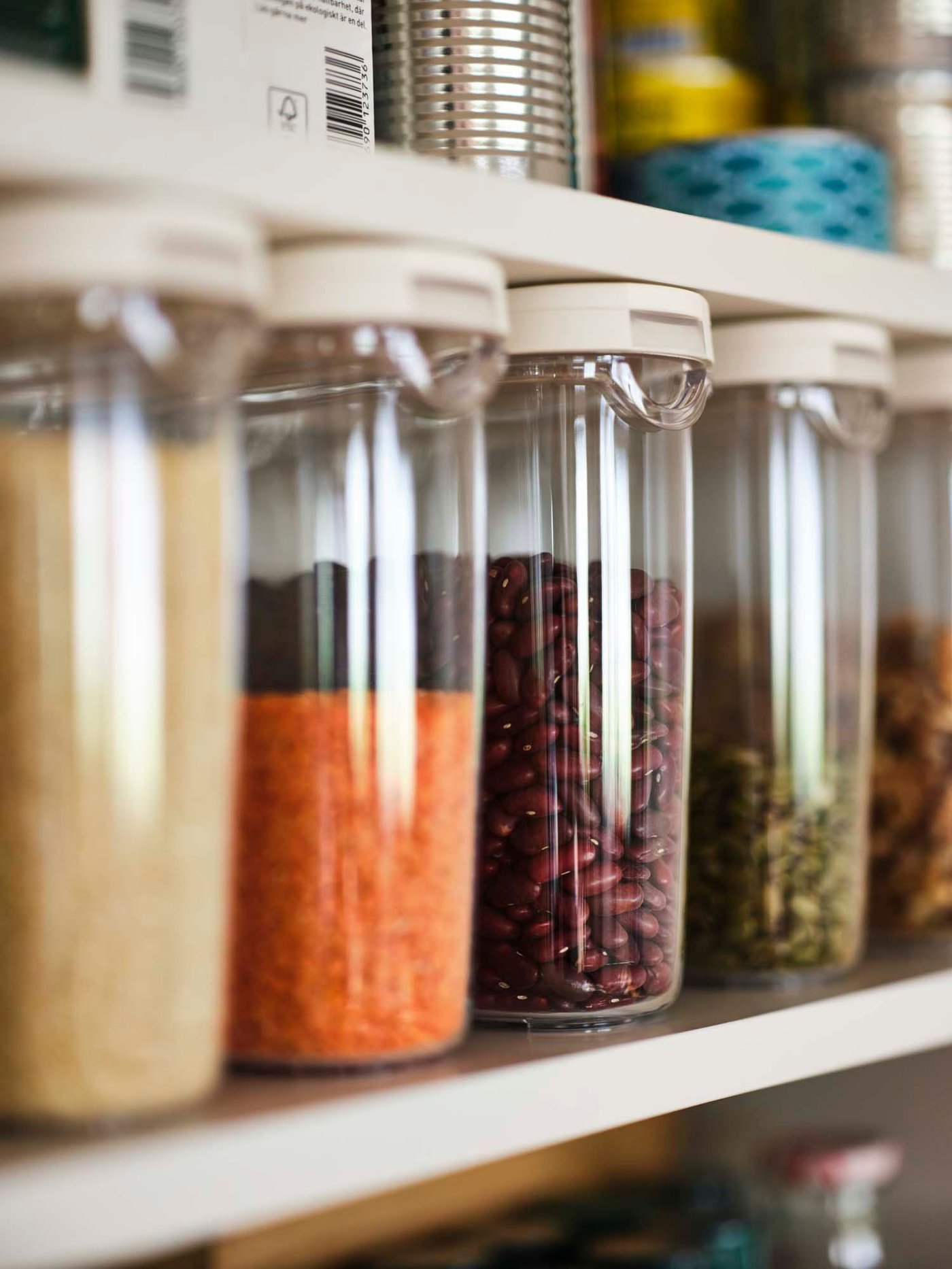Four transparent/white IKEA 365+ dry food jars with lids filled with dry ingredients on a shelf.