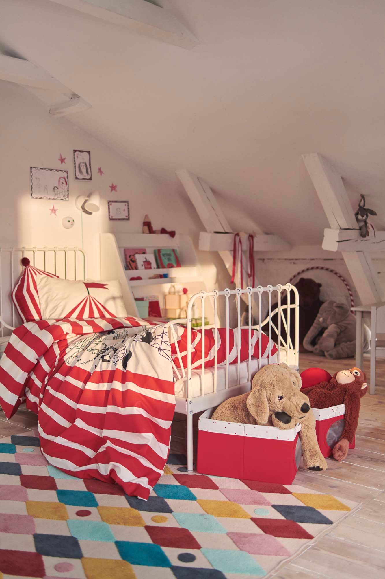 A children's bedroom with a metal bed and circus style bedlinen. On the floor is a harlequin style coloured rug.