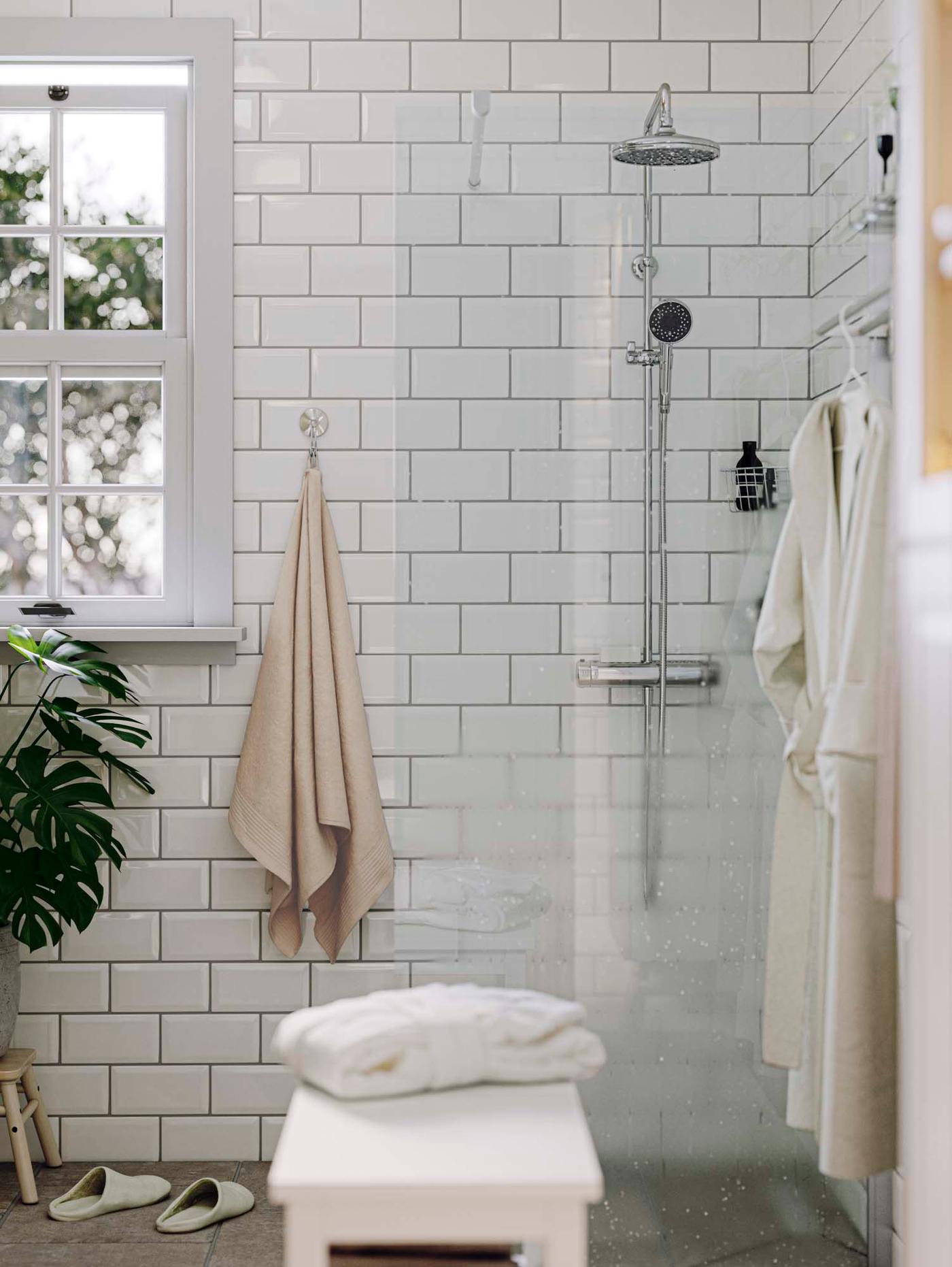 A shower with a glass wall in a bathroom with white subway tiles.