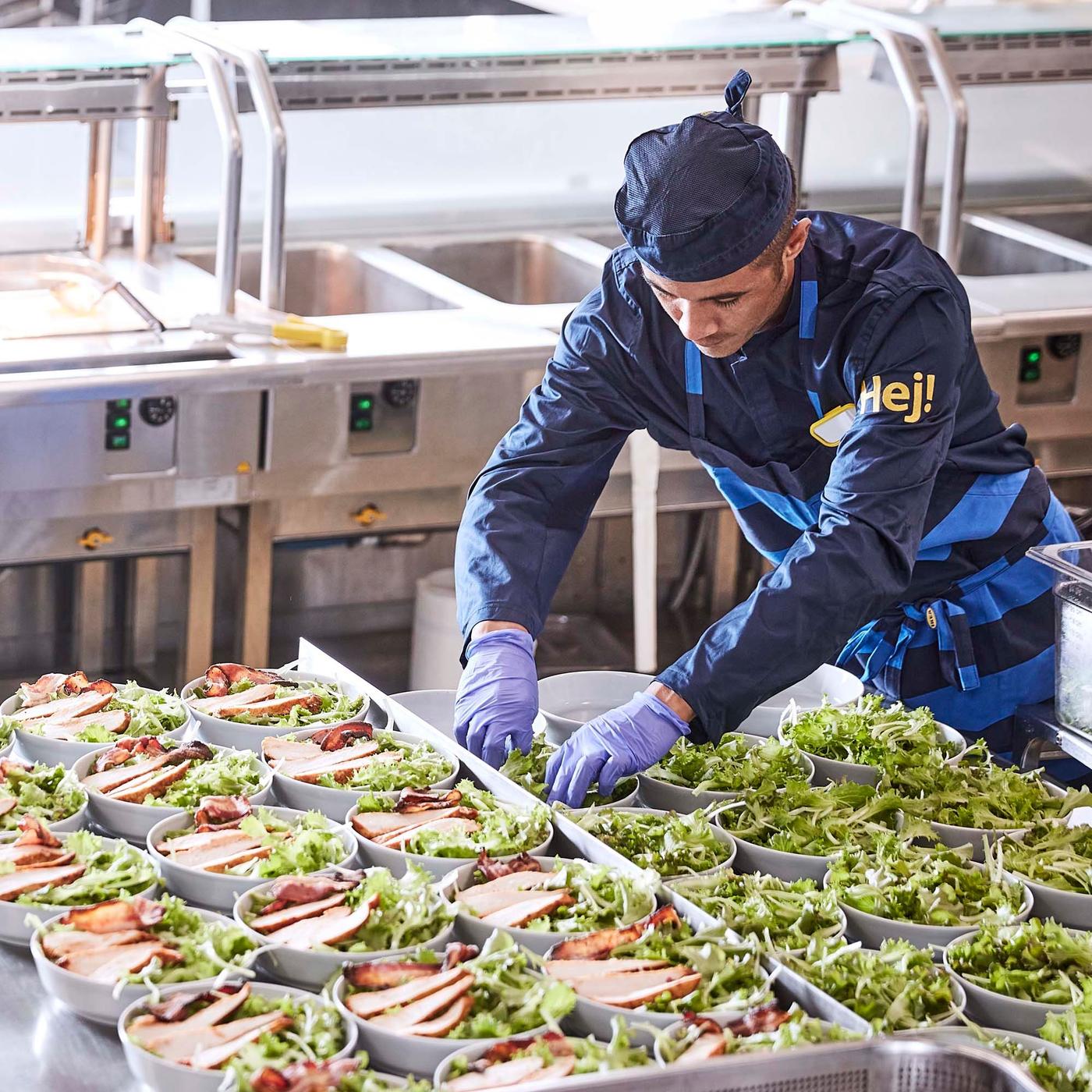 An IKEA restaurant co-worker adds salad leaves to many plates.