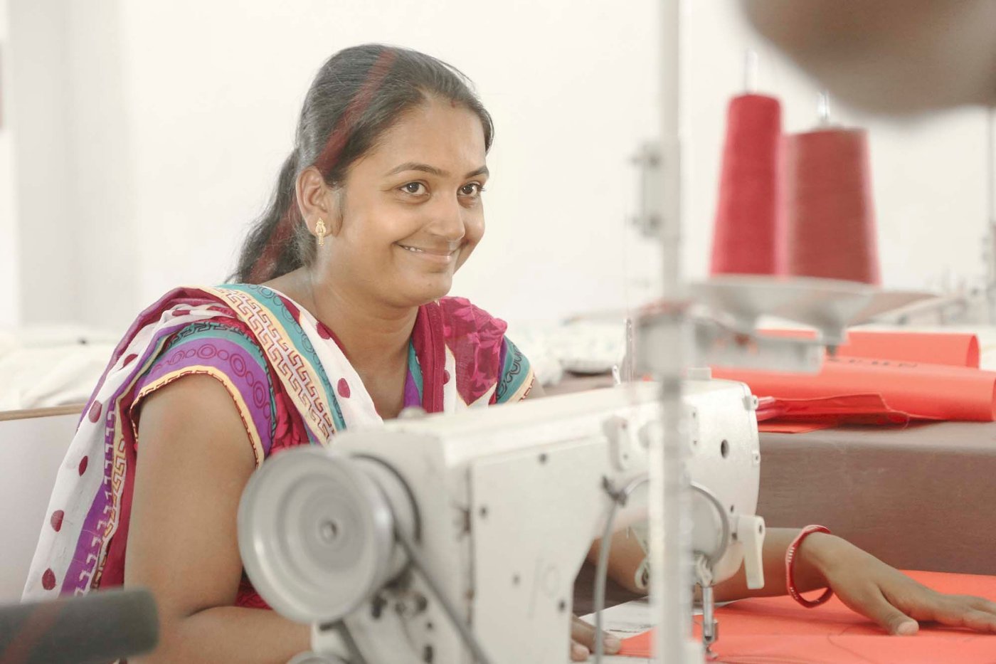 A woman smiles as she works on an electric sewing machine.
