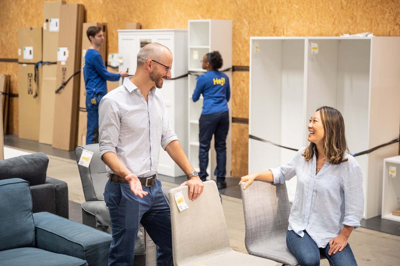 Two people talk in a furniture shop. One is sitting.