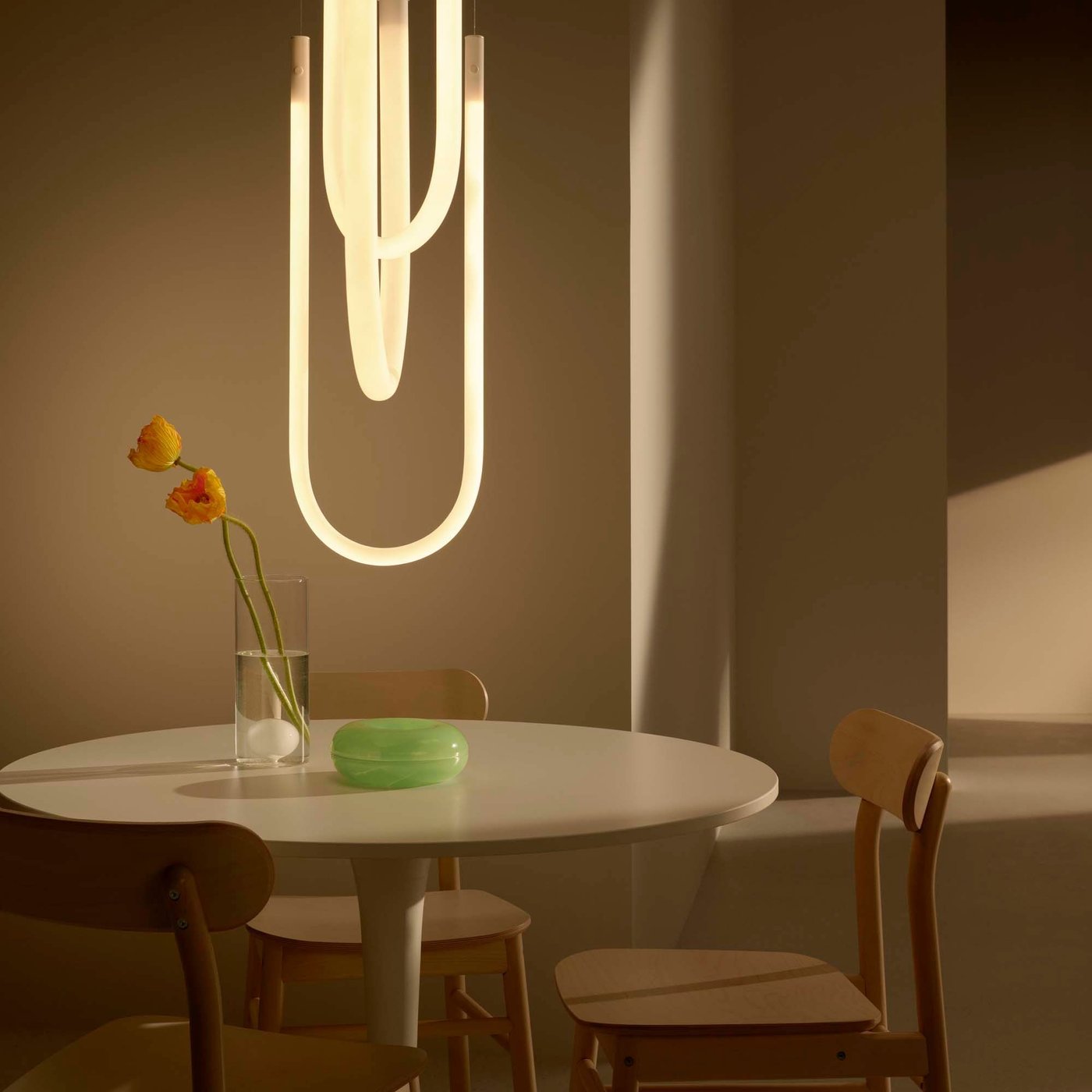 A glowing sculptural ceiling light hangs over a white round dining table.