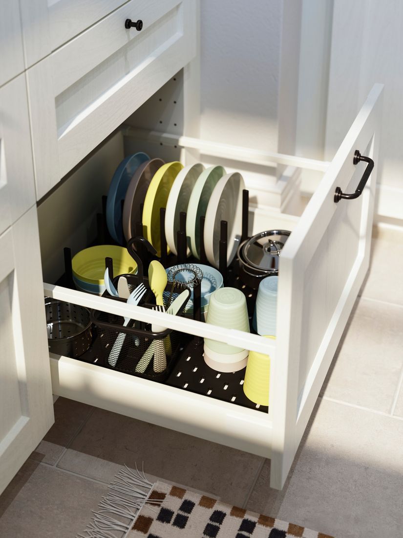 A bottom kitchen drawer packed neatly with children's dinnerware and cutlery.