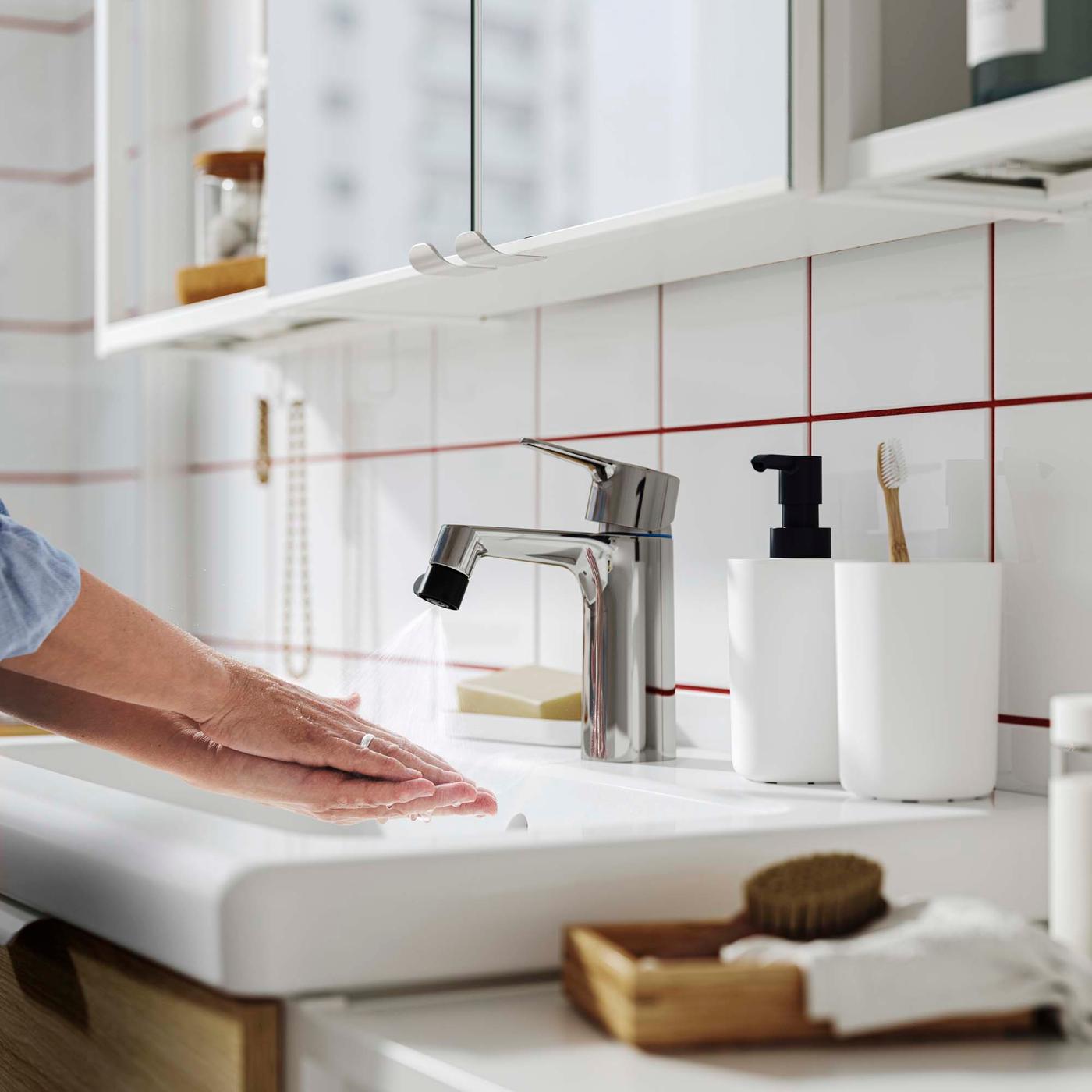 A person washes their hands under a chrome tap fitted with an ÅBÄCKEN nozzle.