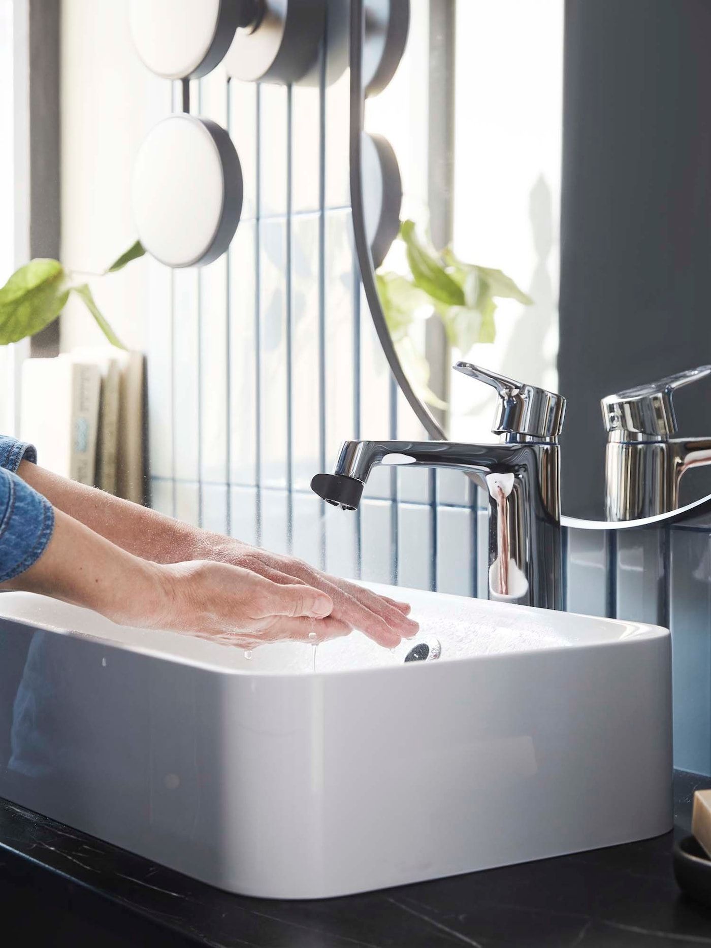 A person washes their hands in a washbasin. The tap has an ÅBACKEN water-saving nozzle attached.