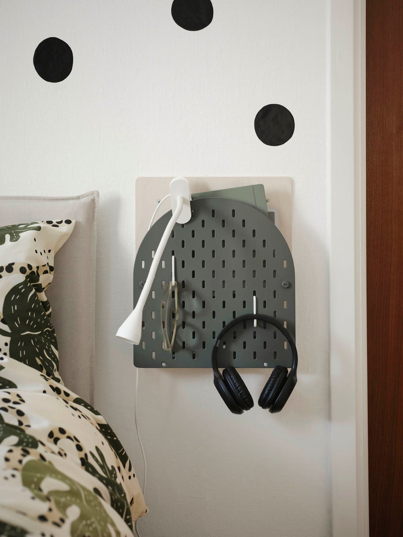 A VATTENKAR wall storage attached to a wall with a white lamp clamped to it and headphones hanging from a hook.