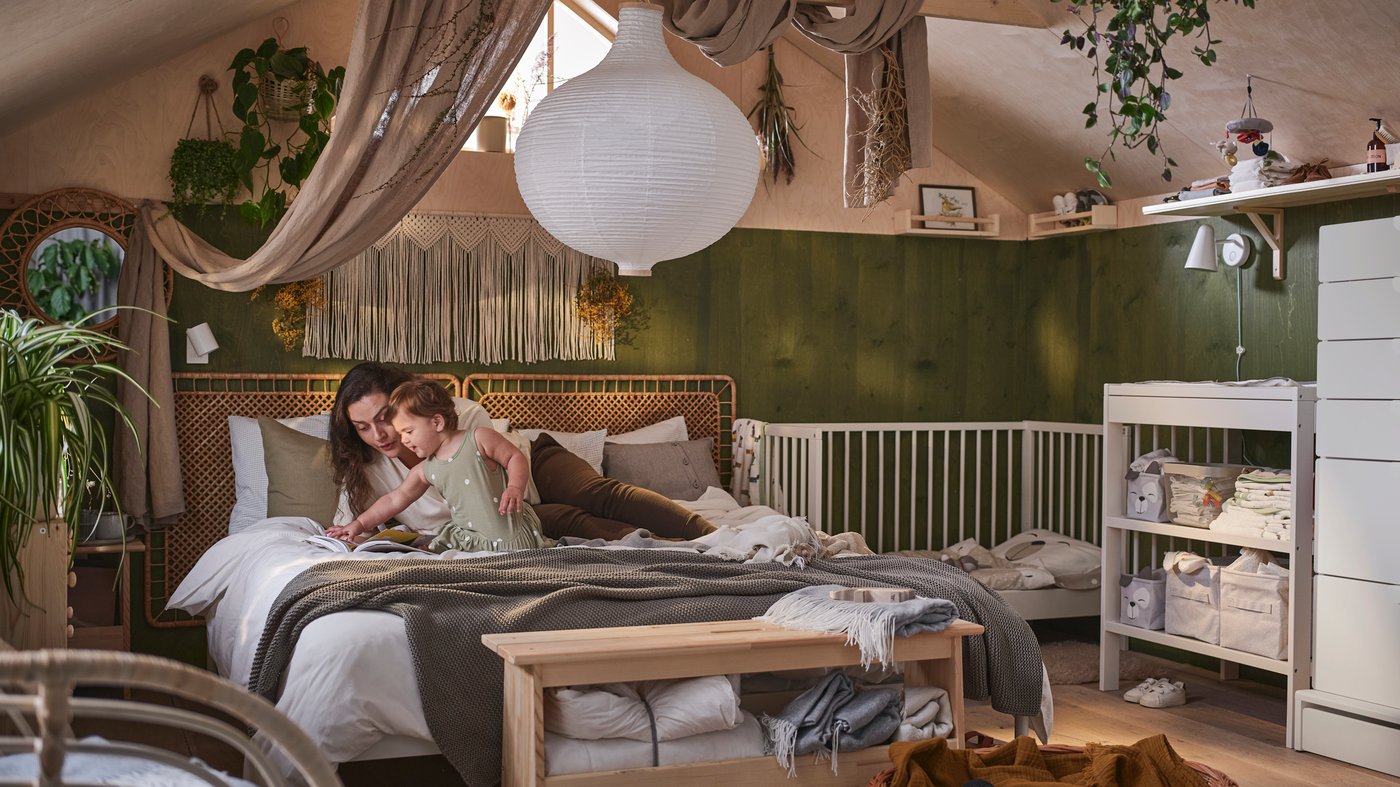 A parent and child sitting on a bed and looking at a book in a dark green and pink bedroom with a sloped ceiling.