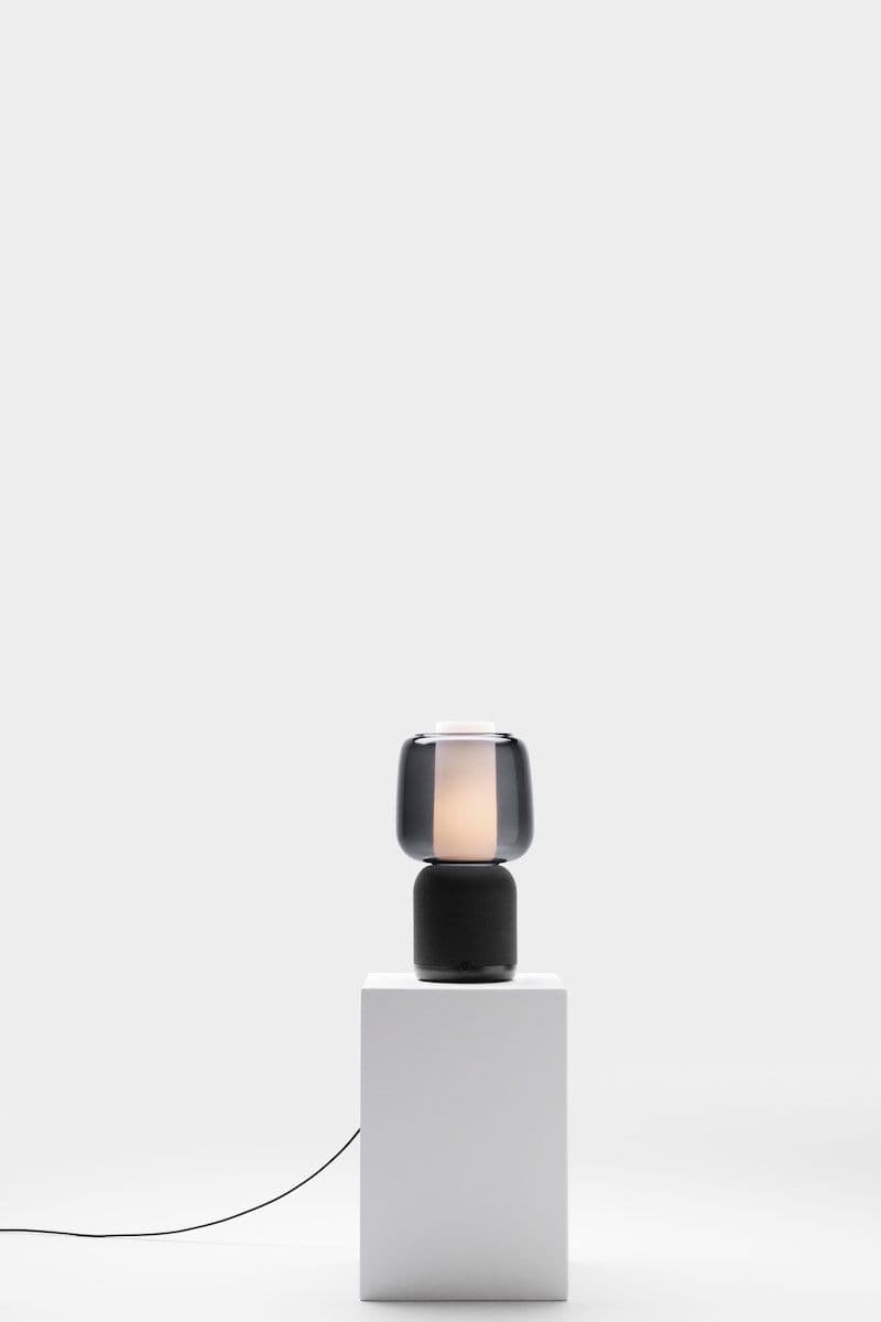 The SYMFONISK speaker lamp with Wi-Fi and glass shade on a white plinth in a white studio setting.