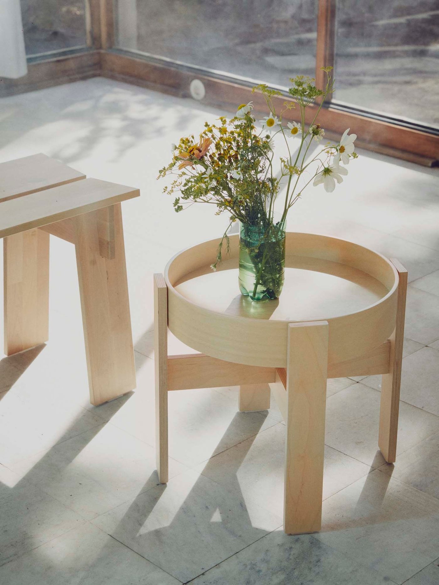 A table and bench from the BASTUA collection stand in a room. The sun is shining on them, creating reflections.