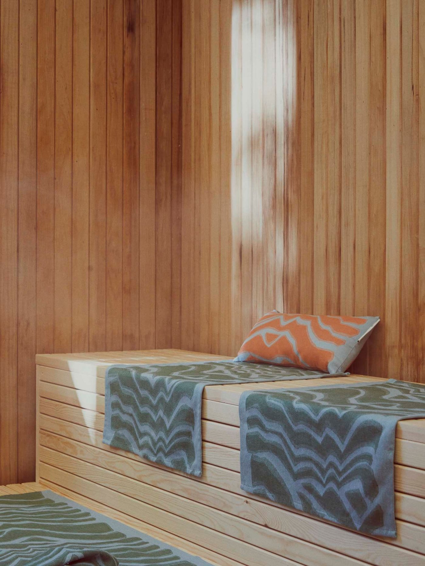 A sauna with three towels and a cushion from the BASTUA collection.