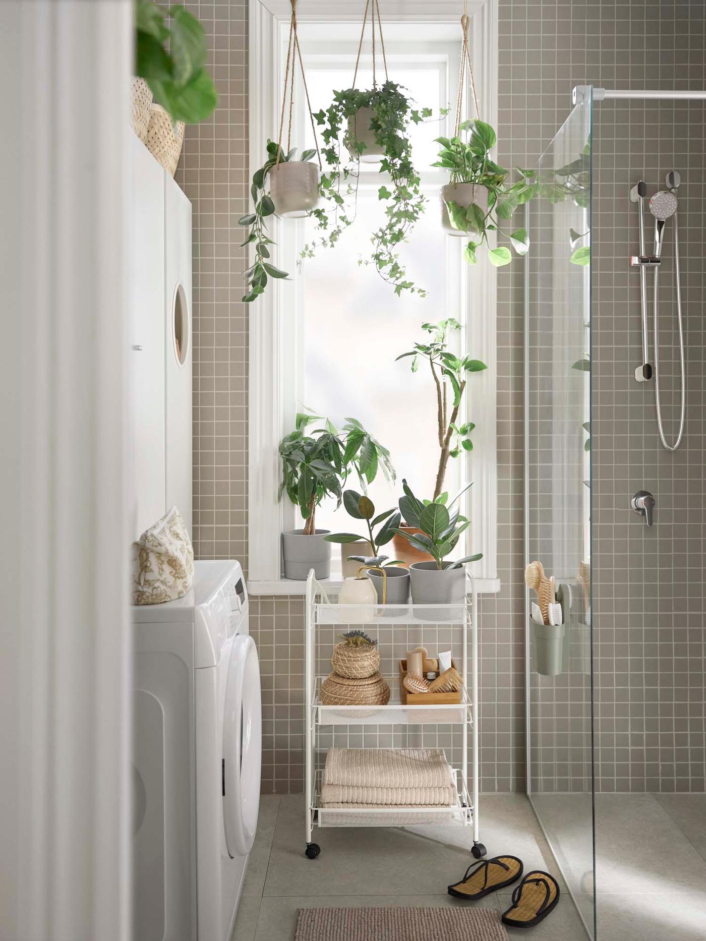 Plants surrounding the window beside a shower in a white and grey bathroom.