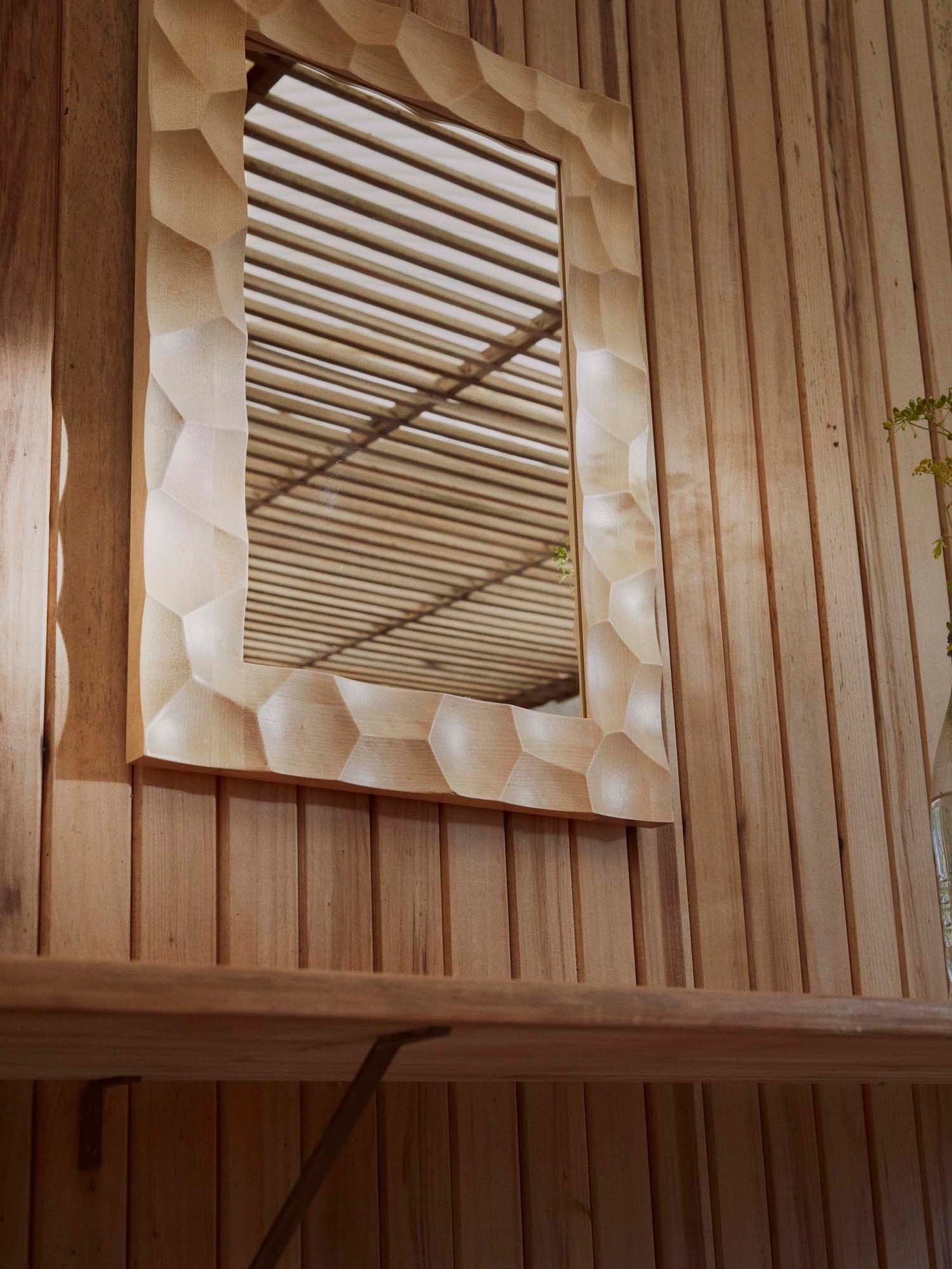 A wood framed mirror from the BASTUA collection on a wood panel wall.