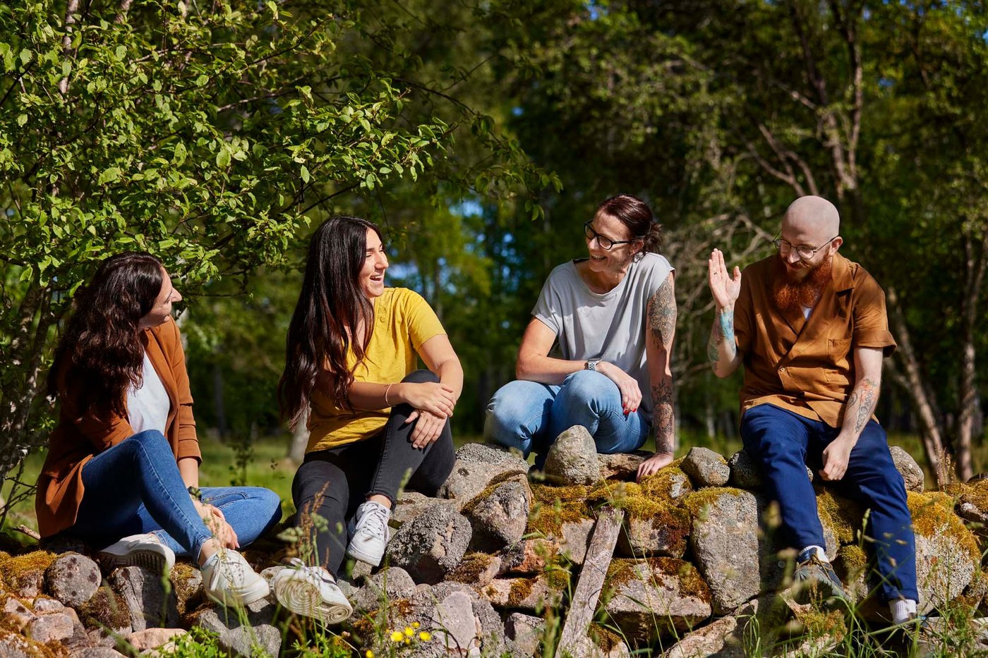 Four co-workers laughing together while they sit in the sun on an old stone wall with the forest behind them.