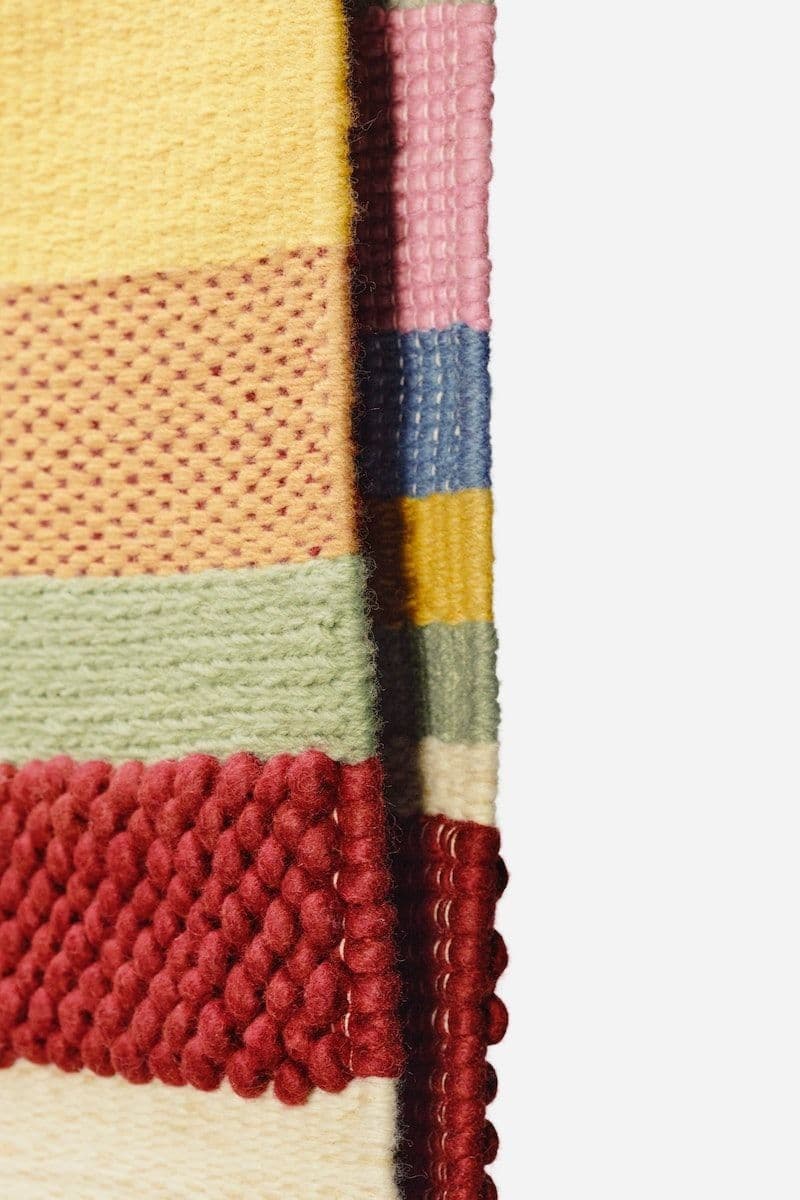 A folded edge of a BRÖNDEN rug, with all seven colours and weaving techniques visible.