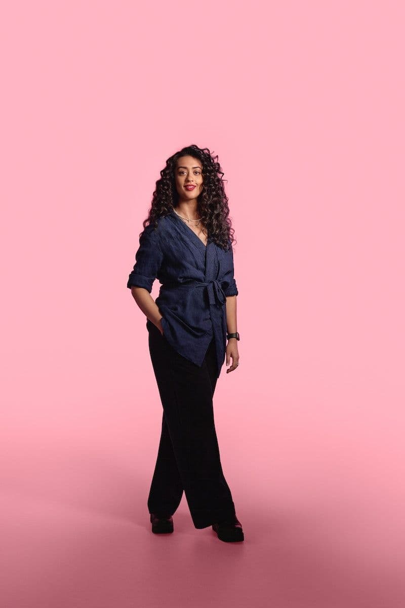 Designer Akanksha Deo standing against a pink infinity background.