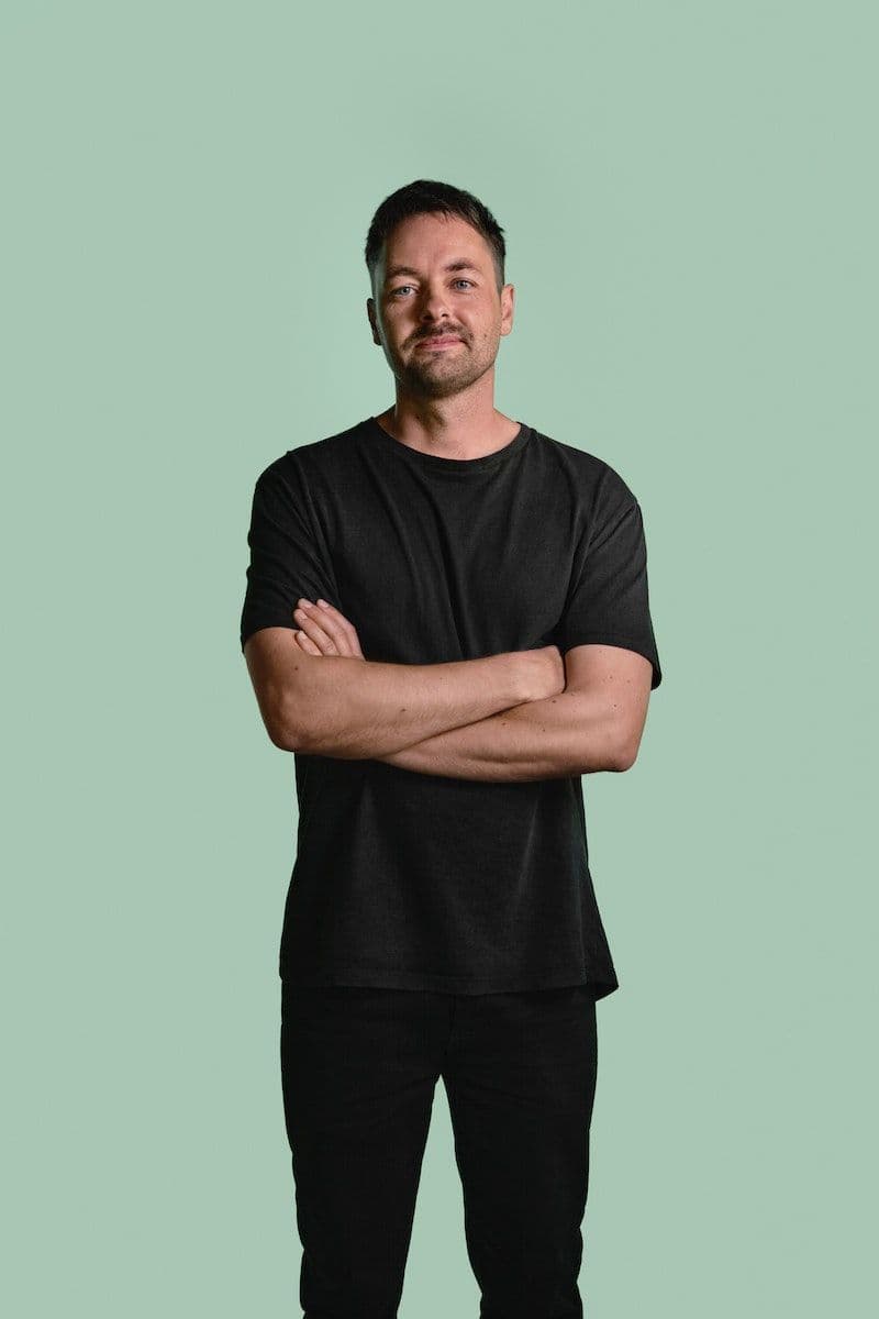 Mikael Axelsson stands on a green backdrop, wearing a black shirt and pants with arms folded.