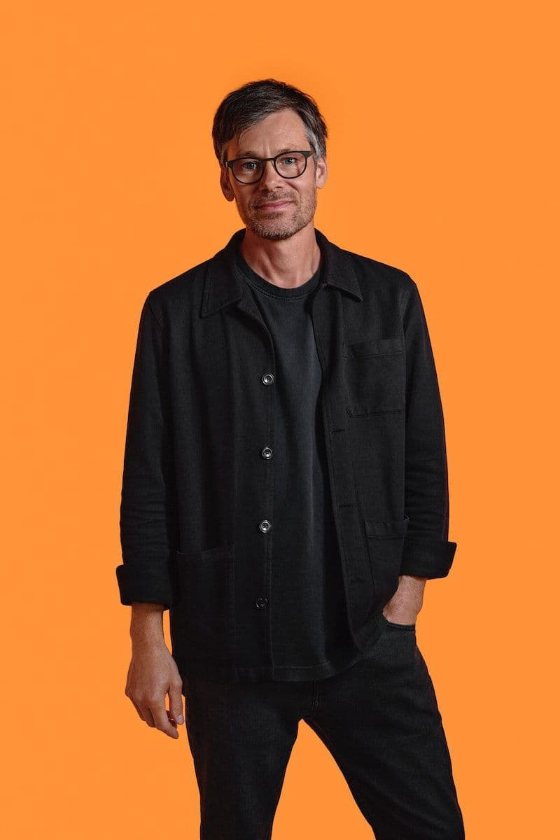 IKEA designer Andreas Fredriksson dressed in black with a bright orange background.