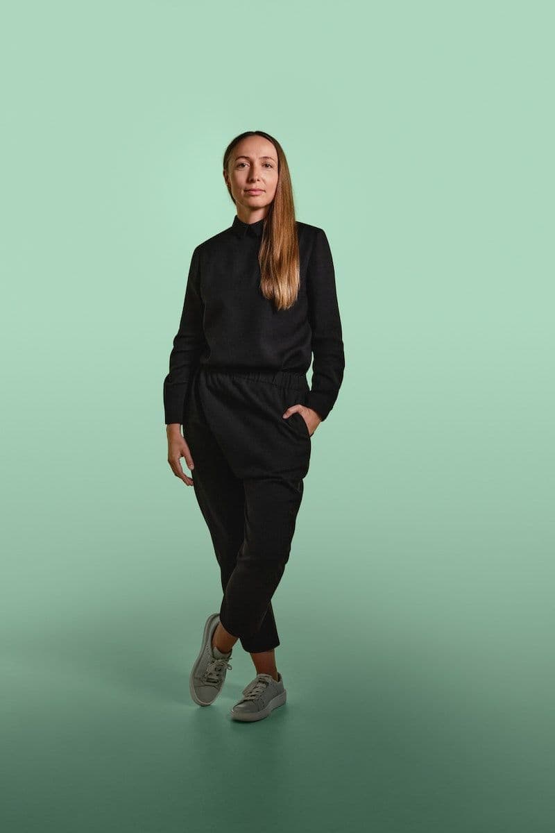 Maja Ganszyniec stands against a green infinity backdrop, wearing a black blouse and trousers.
