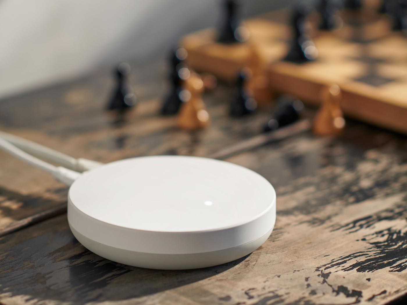 A DIRIGERA hub for smart products is placed on a wooden table, next to a chessboard.