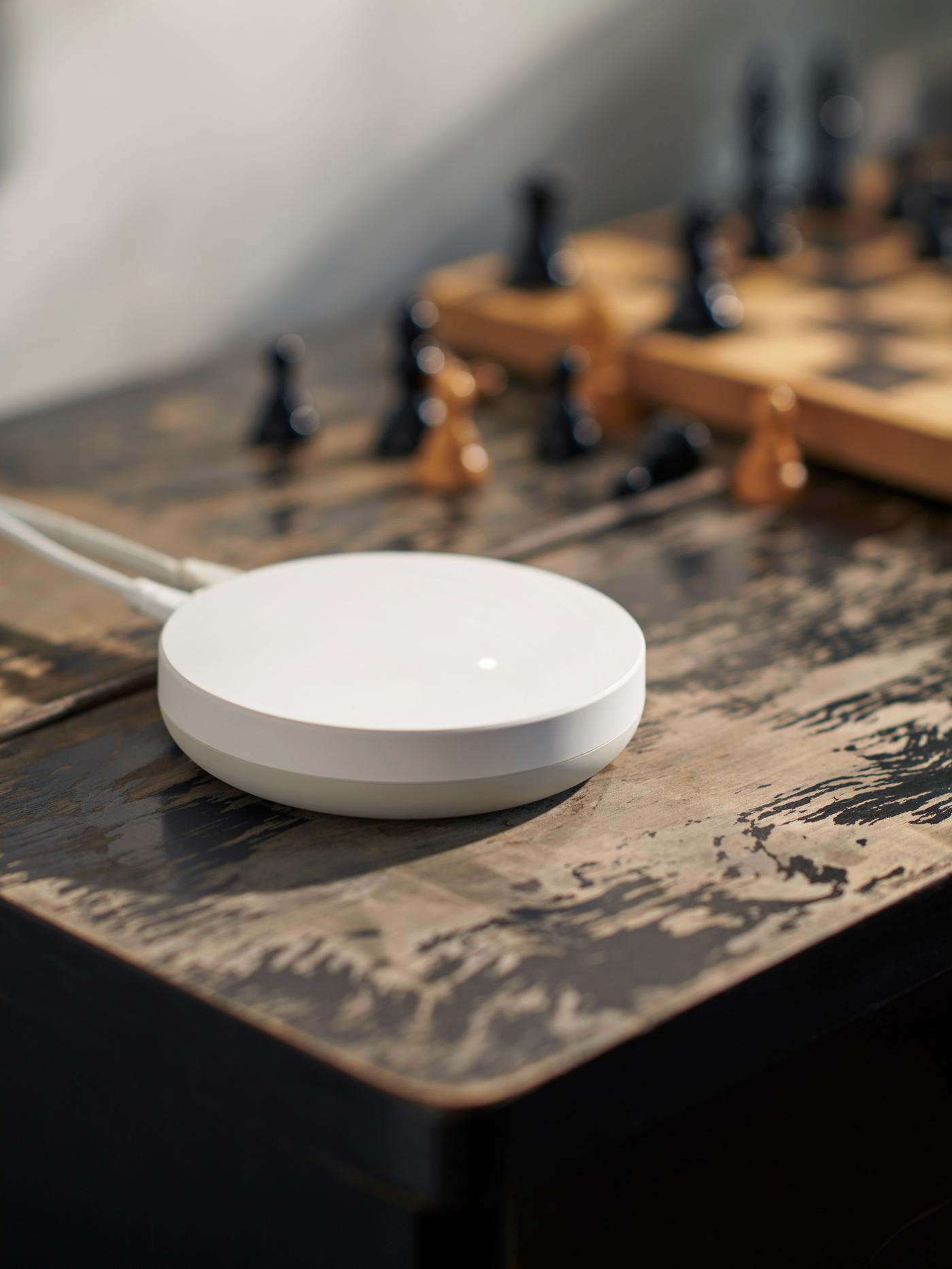 A DIRIGERA hub for smart products placed on a wooden table, next to a chessboard.