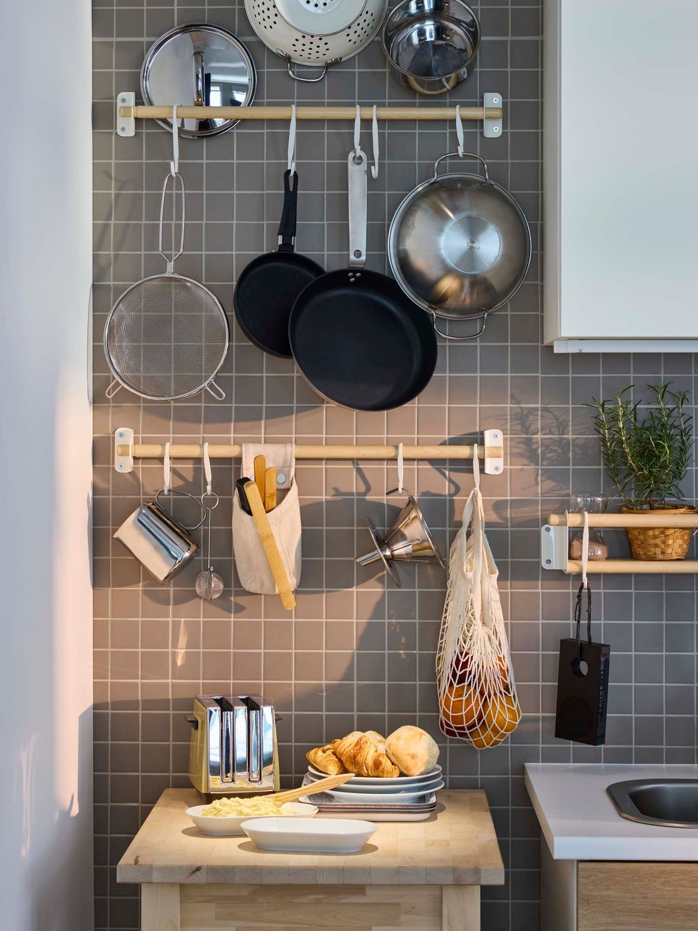 A kitchen with pans and other kitchen items hanging on hooks from two birch NEREBY rails attached to a tiled wall.