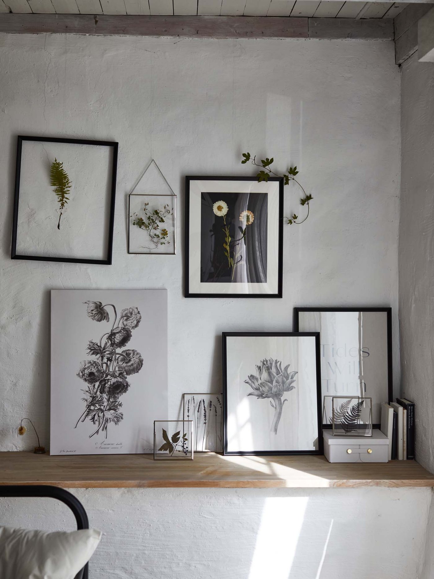 Assorted frames containing sketches, photos and dried flowers hang from a wall or rest on a shelf in a rustic style setting.