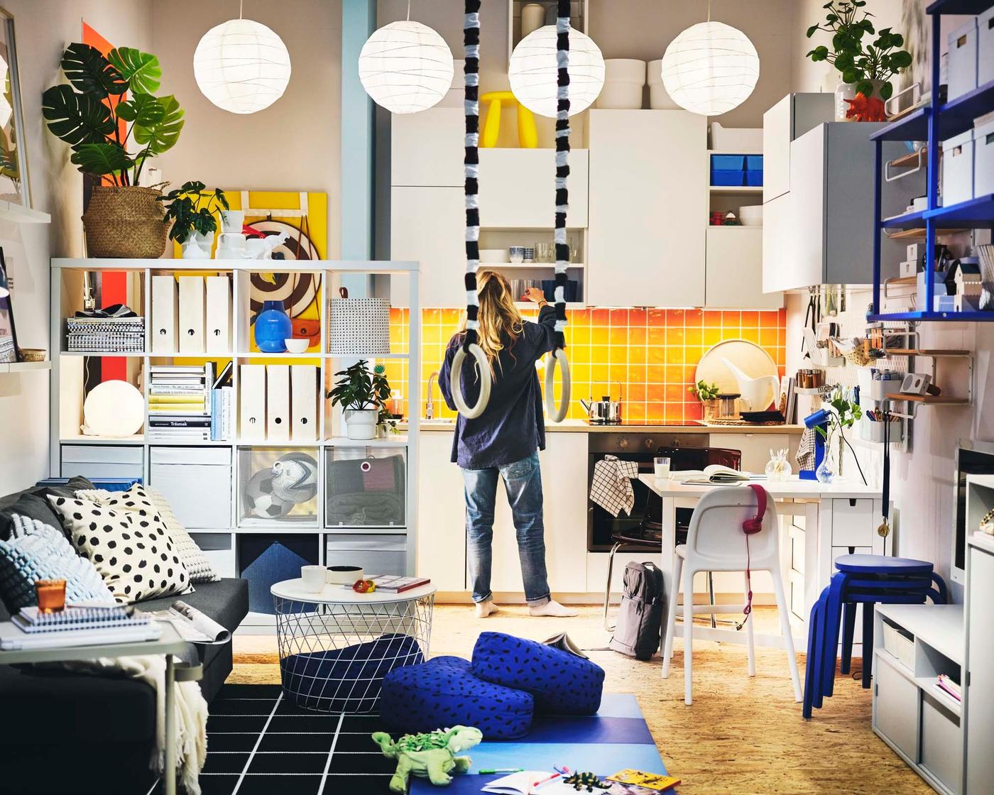A person stands in a colourful, compact apartment with a living and dining area and kitchen.