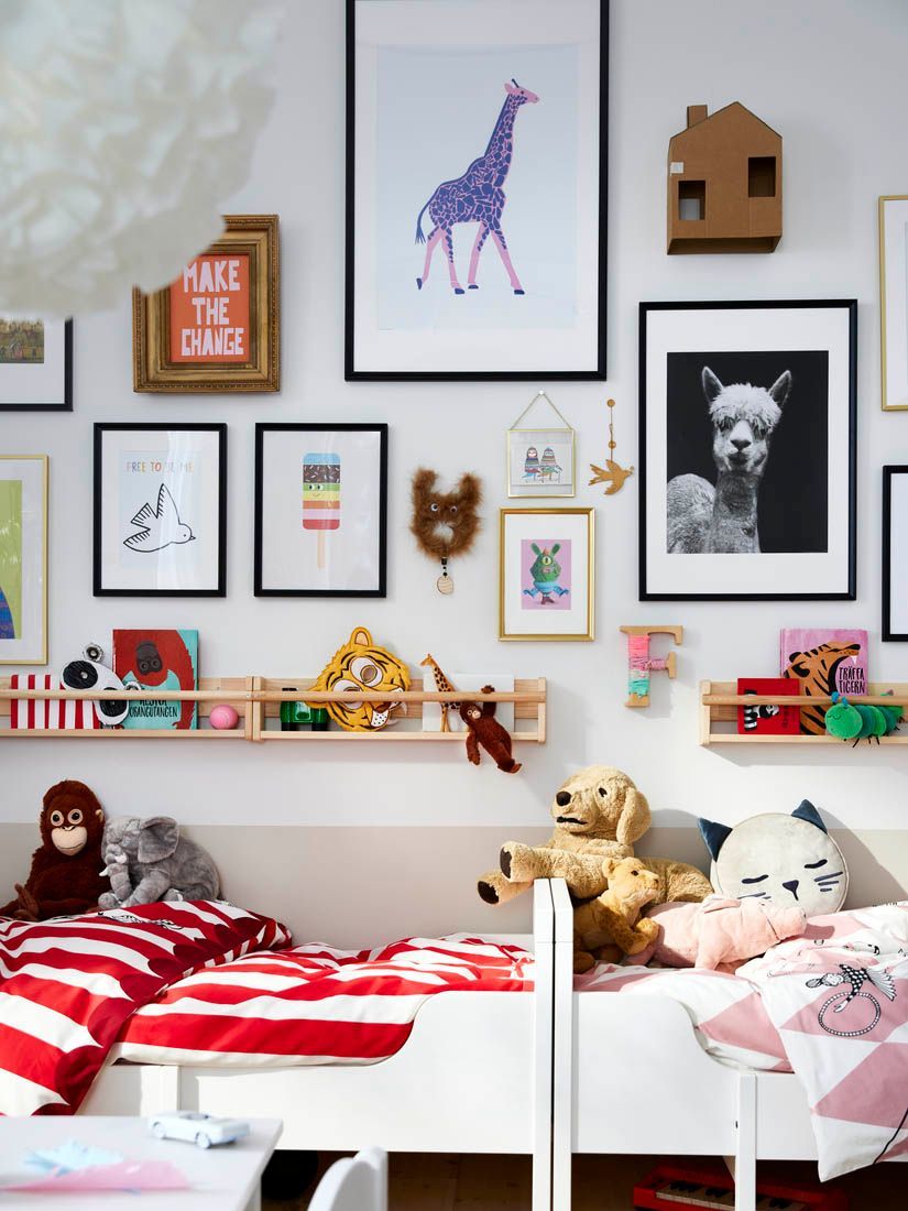 Playful children's room with a wall full of art and ornaments and two children's beds placed end to end.