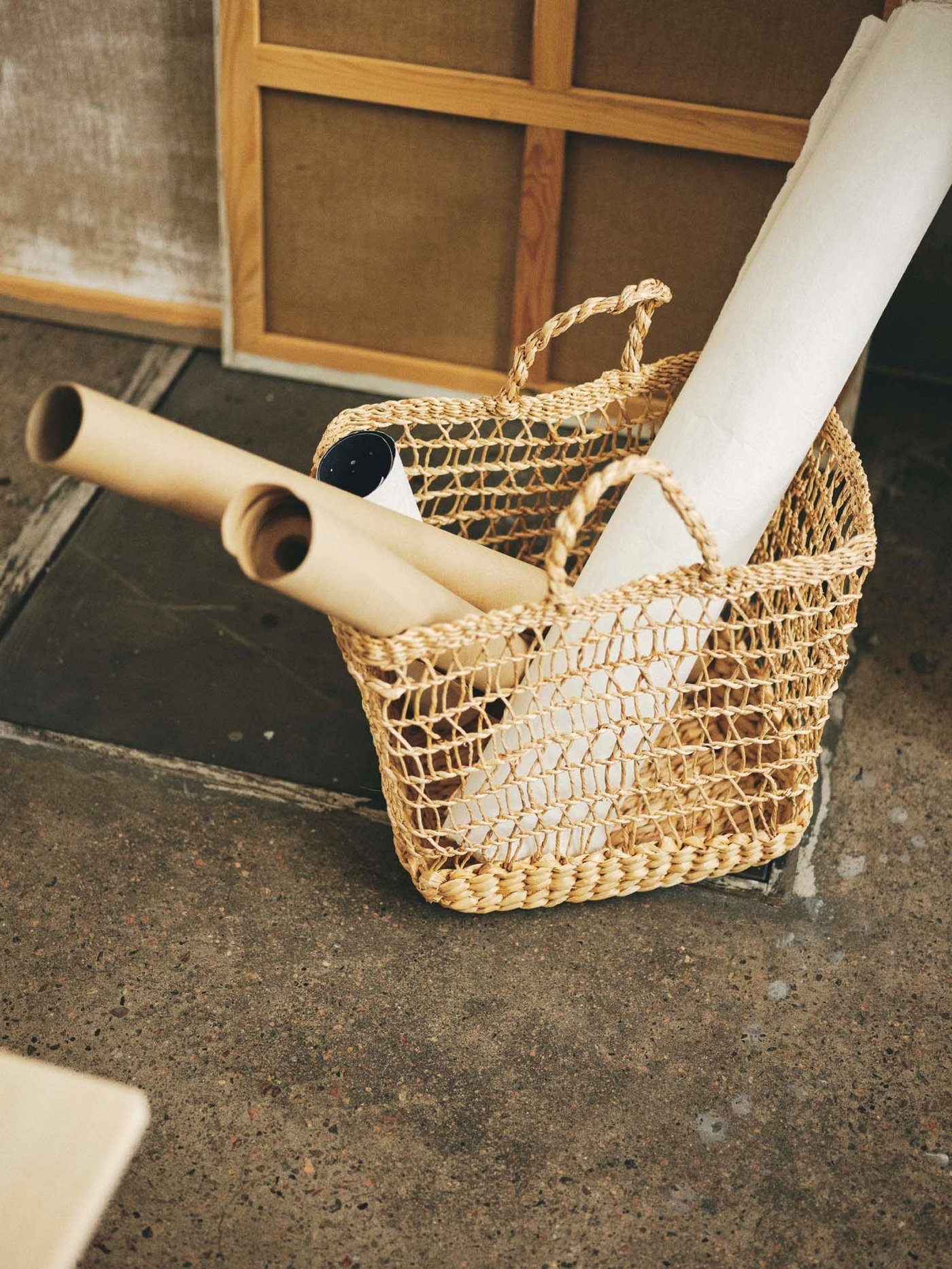 A handmade shopping basket sits on the floor. It contains rolls of paper.