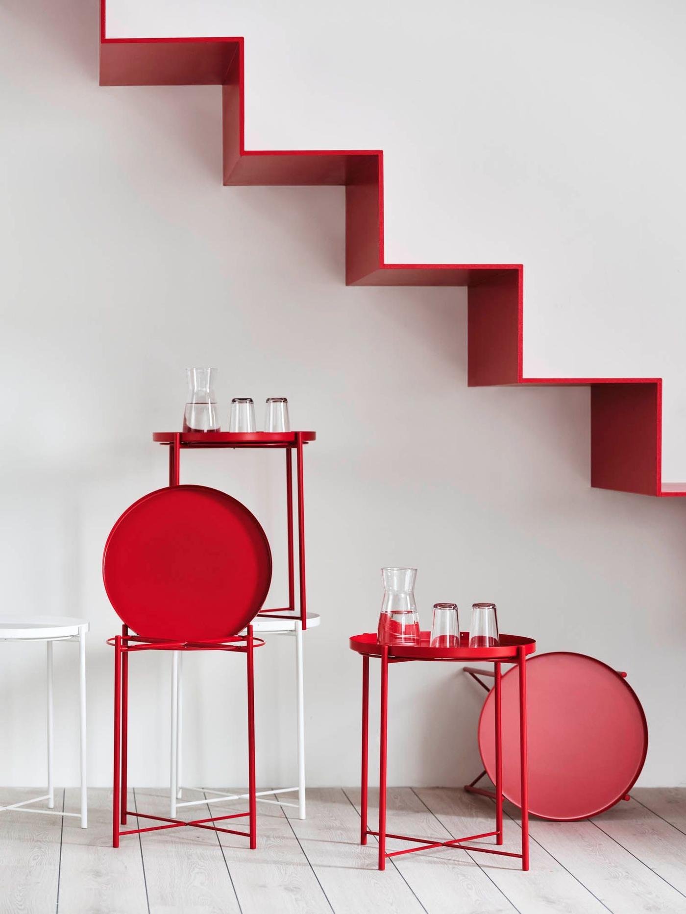 Below a red floating staircase against white walls and floors are an assortment of red and white GLADOM tray tables.