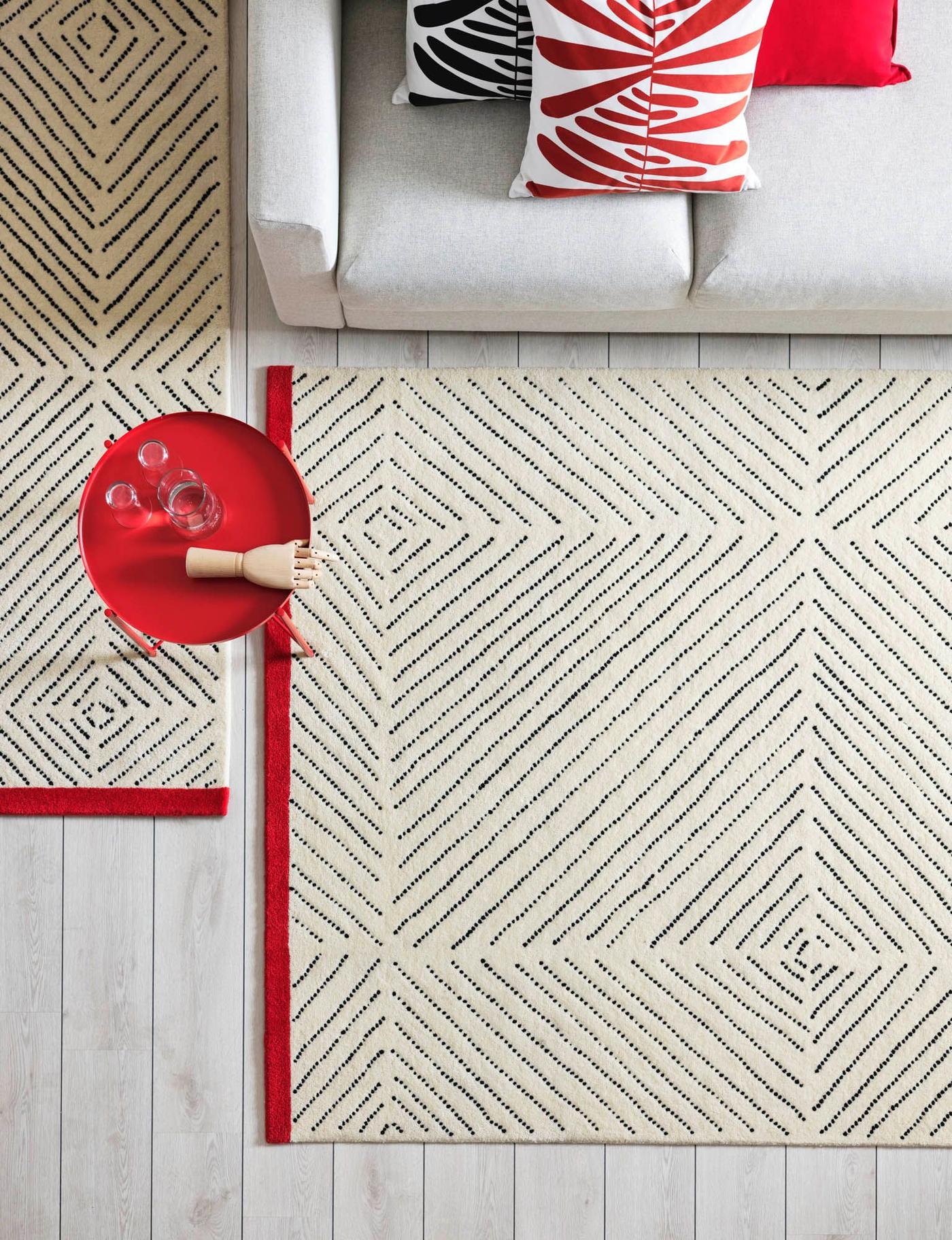 Aerial view of a living room with two UNDERVISNING rugs, a white sofa, and red GLADOM tray table.