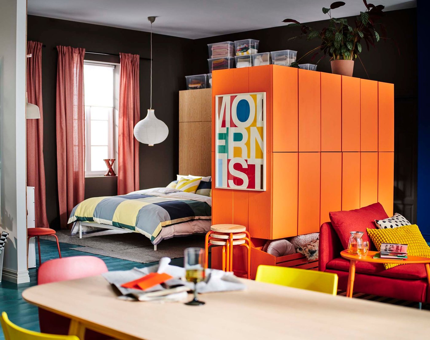 View from the kitchen, with a bed and bright orange units. There is also a red sofa.