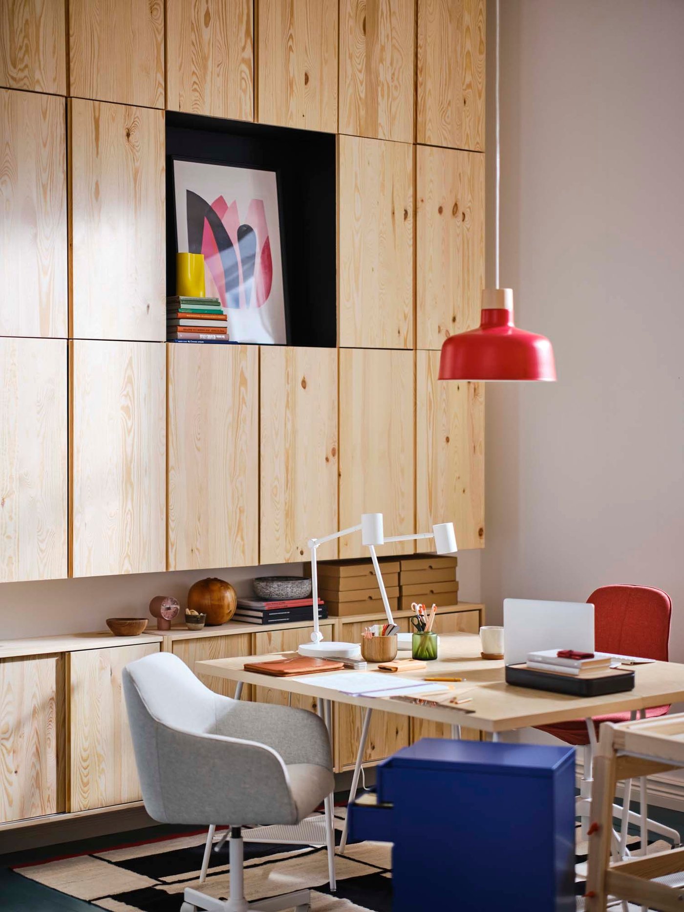 A home office area with light wood fronted cupboards on the wall, a wooden desk and a blue filing cabinet.