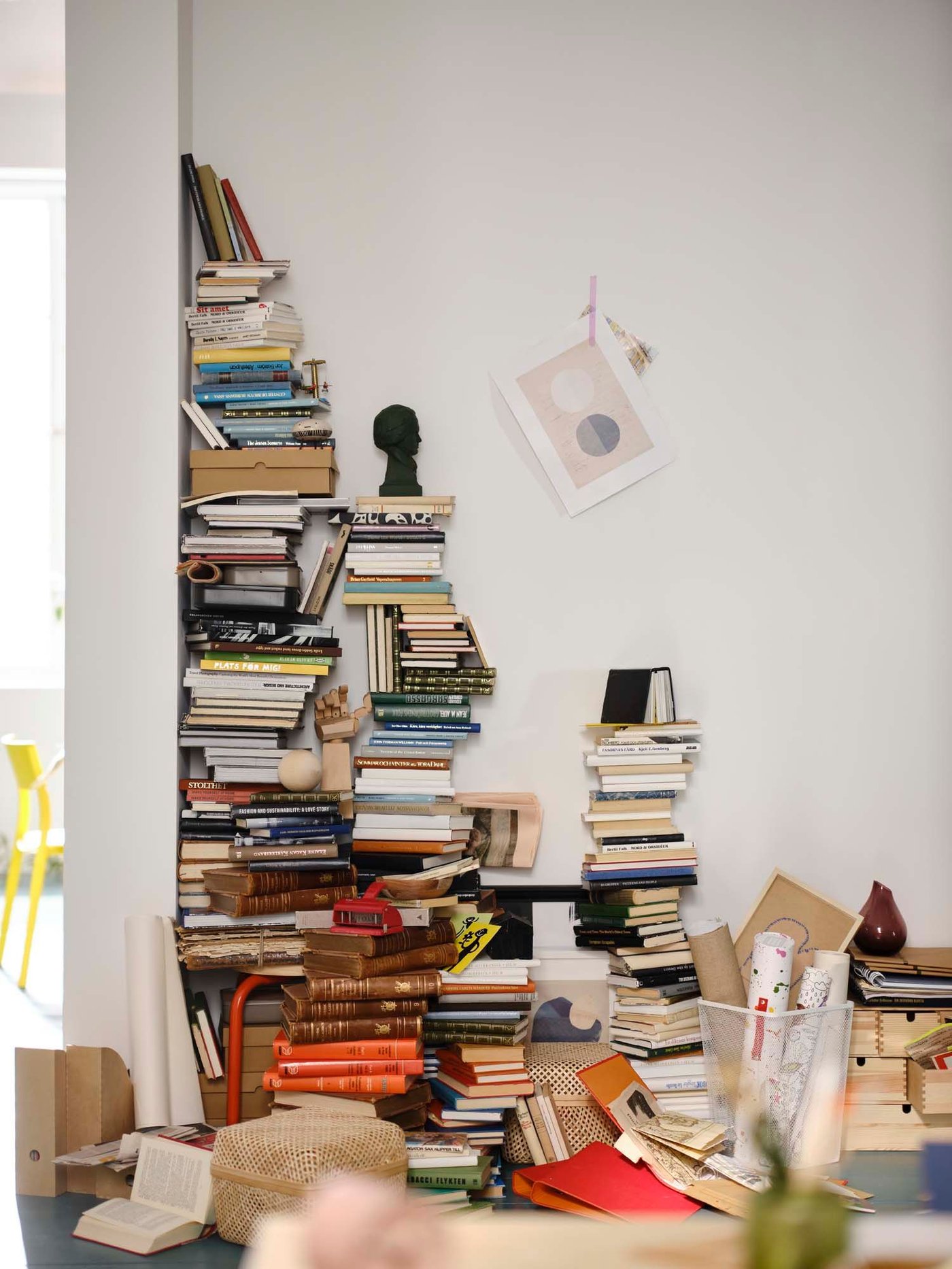 Piles of books are stacked in a messy pile against a white wall.