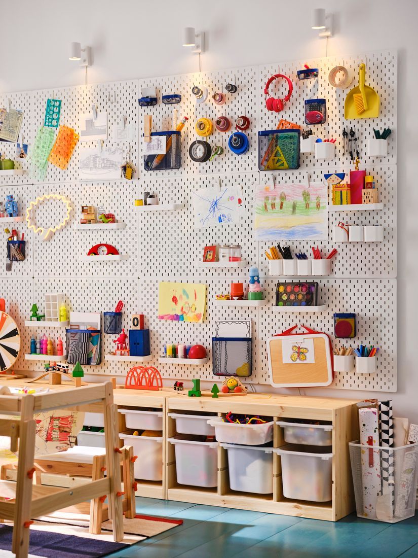 A wall storage organiser filled with pots and hooks holding drawing tools, etc.