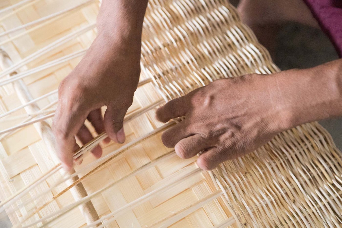 A pair of hands weave a rattan basket.