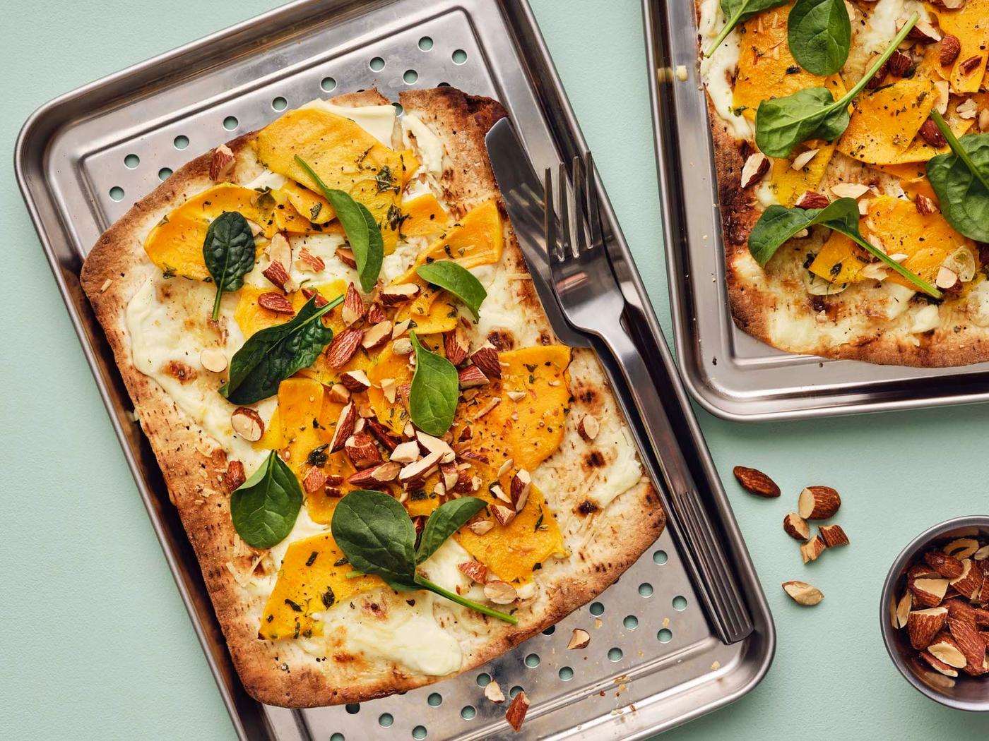 A pumpkin pizza on a metal tray, on a light green surface.