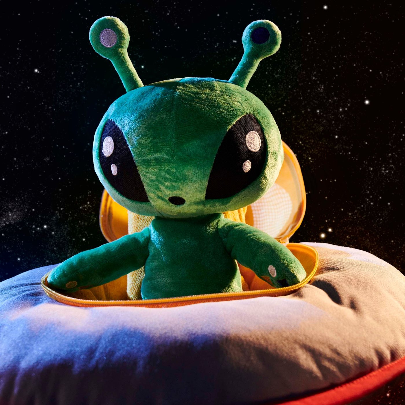 A green toy alien sits in a soft spaceship. 