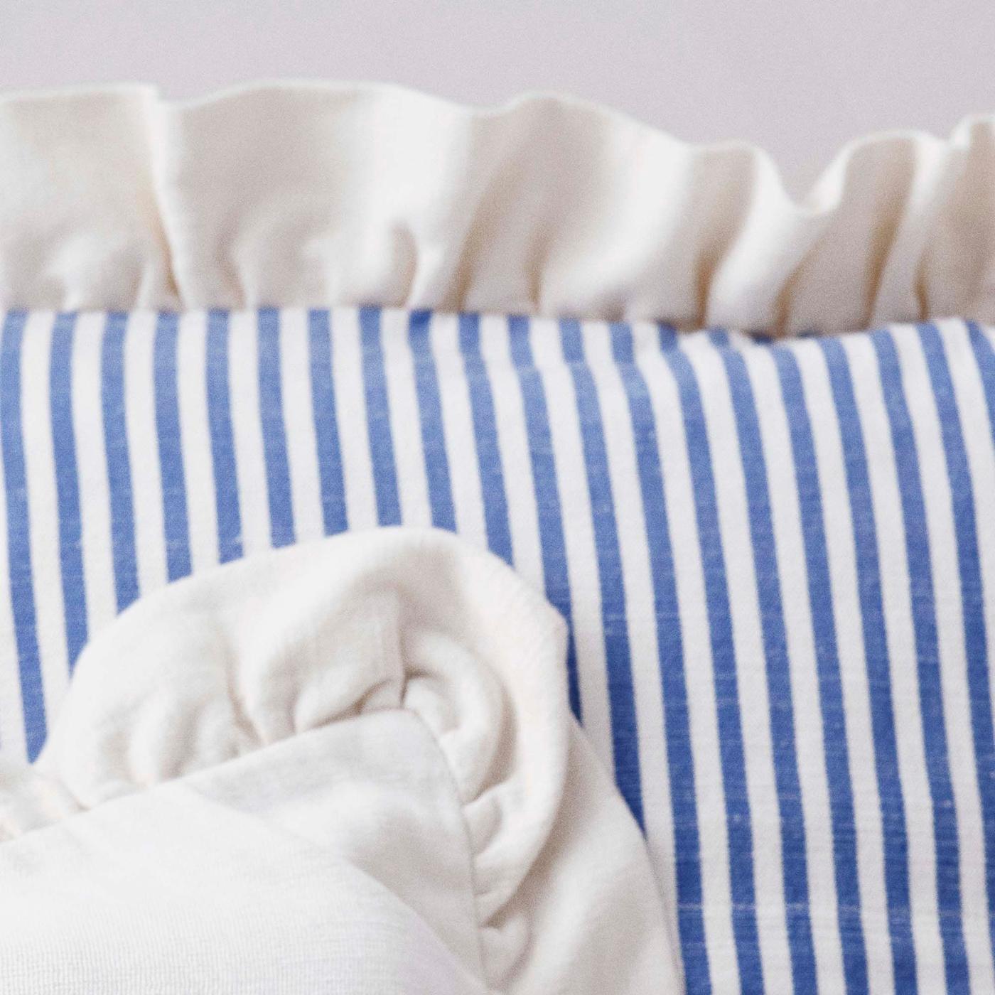 A close-up of a corner of a blue and white striped ÅKERNEJLIKA cushion. It has cream ruffles around the edges.