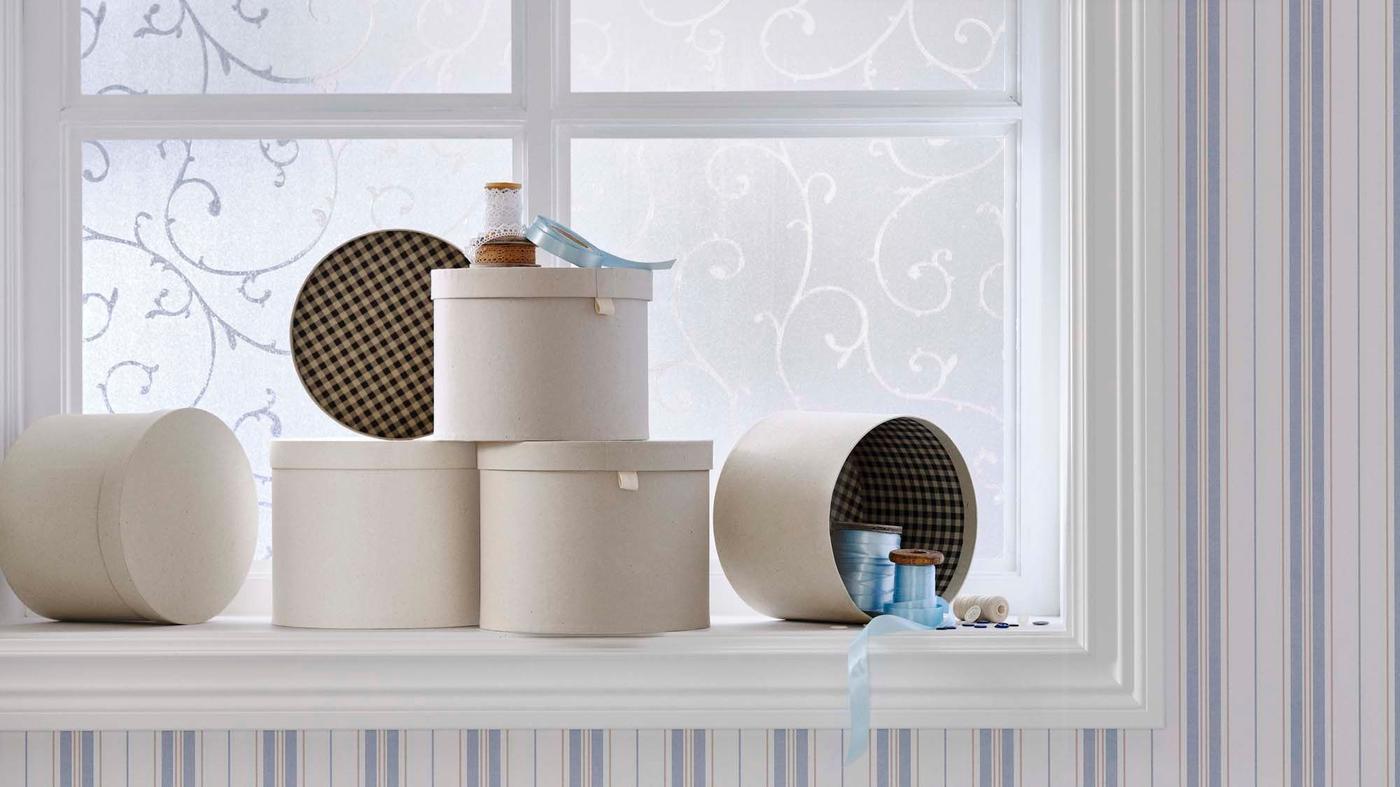 A collection of round RÅGODLING storage boxes sit on a windowsill. One is stacked and one is open.