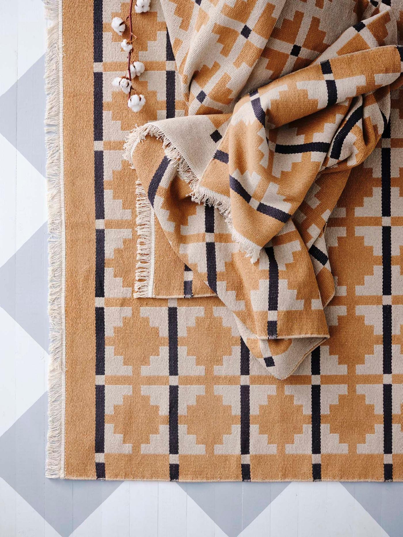 The corner of an ochre, black and cream patterned rug on a blue and white check floor.