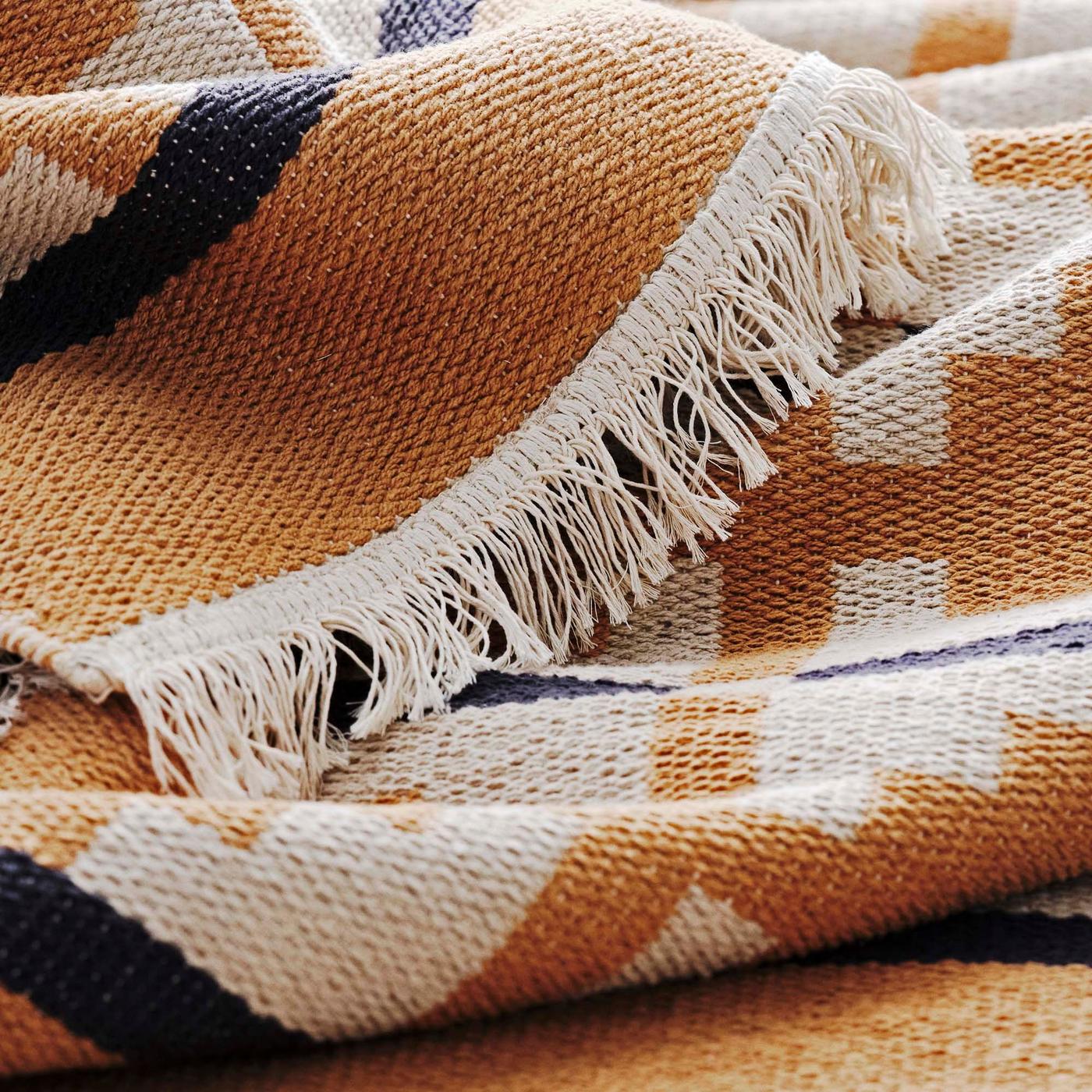 A close-up of the edge of a mustard, black and cream rug with a fringed edge.