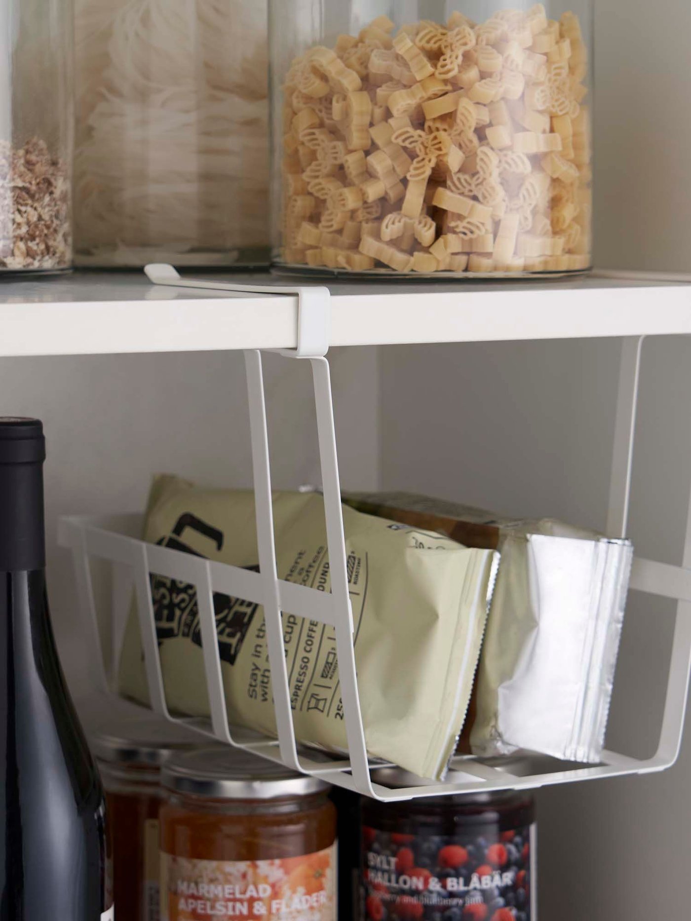 A shelf with a PÅLYCKE clip-on basket holding two bags of ground coffee.